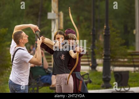 Omsk, Russland. 9. Mai 2021. Vorbereitung für eine Masse Bogenschießen Flash Mob. Der Kerl macht ein Foto am Telefon von seiner Freundin mit einem Bogenschießbogen und einem tr Stockfoto