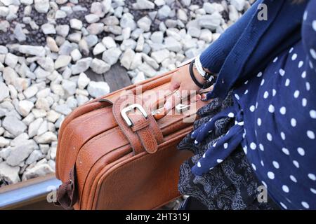 Nahaufnahme einer Person, die einen Lederkoffer in der Hand hält, der auf Bahngleisen läuft Stockfoto