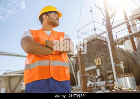 Selbstbewusster junger Arbeiter, der am Industriestandort steht Stockfoto