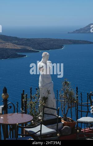 Santorini, Griechenland : May 10, 2021 : eine Terrasse mit Tischen, Stühlen und einer griechischen Statue über die Ägäis in Santorini bietet einen fantastischen Blick auf die Ägäis Stockfoto