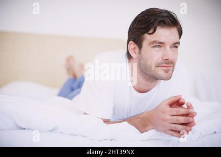 Denken wir über einige Dinge nach Ein hübscher junger Mann, der auf seinem Bauch auf einem Bett liegt und nachdenklich aussieht. Stockfoto