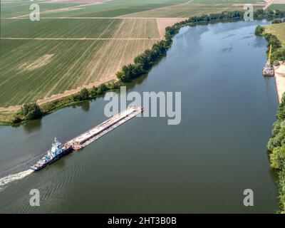 Kleines Schleppboot schiebt Barge entlang ruhigem Wasser vorbei an Feldern Stockfoto