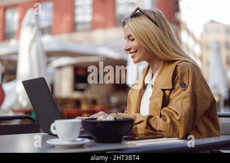 Porträt einer charmanten Frau, die draußen auf einem Laptop arbeitet Stockfoto