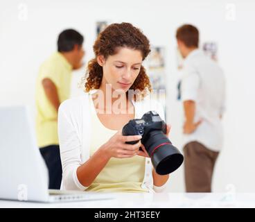 Frau, die Bilder in der Kamera auscheckte. Die Fotografin sieht sich Bilder in der Kamera an, die Kollegen im Hintergrund. Stockfoto