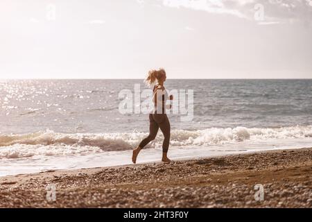 Athletische Frau, die am Strand auf dem Seeweg läuft Stockfoto