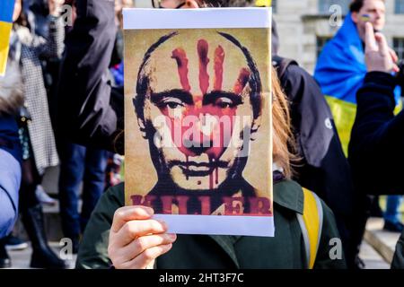 26.. Februar 2022: Ukrainische Staatsbürger und pro-ukrainische Anhänger versammeln sich in Whitehall, um gegen die russische Invasion in der Ukraine zu protestieren. London, Großbritannien. Im Bild: Eine Frau hält ein Plakat mit einem Bild des russischen Präsidenten Putin mit einem blutigen Handdruck auf seinem Gesicht. Stockfoto