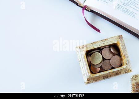 Münzen in einer goldenen Schachtel mit offenem Bibelbuch auf weißem Hintergrund. Das biblische Konzept des christlichen Gebens, Zehnten und Opferens in der Kirche. Stockfoto