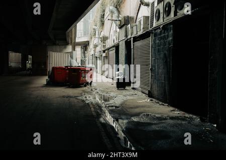 Schmutzige Hintergasse in der Innengasse hinter Bars und Nachtclubgeschäften, große Mülltonnen mit Rädern und Müll auf dem Boden Stockfoto