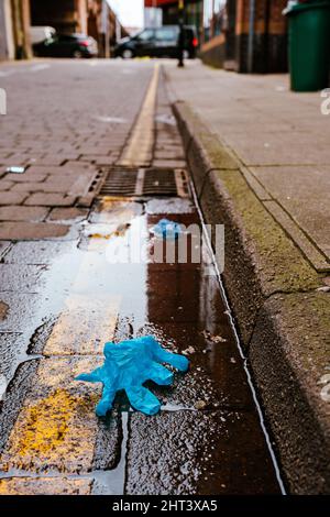 In den schmutzigen Straßen von Manchester wurden Kunststoffhandschuhe verwendet, die in der Rinne neben einer Wasserpfütze und gelben Linien fallen gelassen wurden Stockfoto