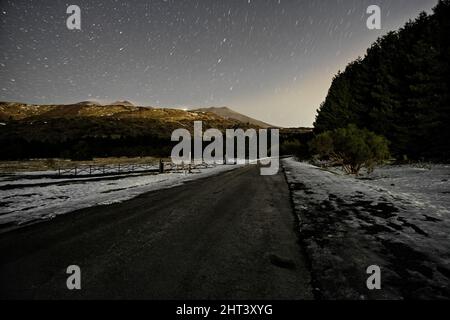 Die Nachtlandschaft in den Bergen ist auf einer gefrorenen Straße zu sehen Stockfoto