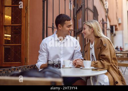 Porträt eines hübschen Paares, das im Café von Außenbeinen sitzt und spricht Stockfoto