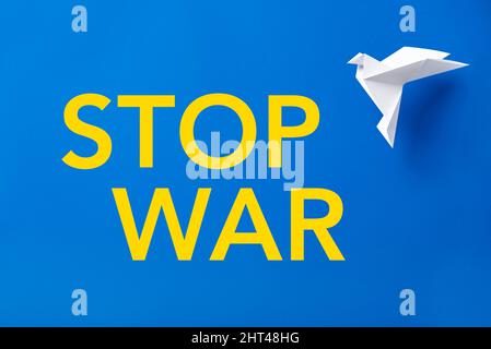 Text Krieg beenden in gelben Buchstaben auf blauem Hintergrund, Farben der ukrainischen Flagge, neben einer weißen Origami-Papiertaube, Symbol des Friedens. Stockfoto