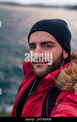 Vertikale Aufnahme eines coolen bärtigen spanischen Mannes, der ein Selfie am See gemacht hat Stockfoto