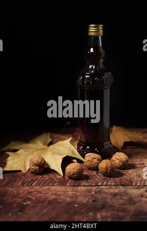 Eine Flasche Walnusswein auf einem Holztisch eingefügt, die Walnüsse und Blätter auf ihm hat Stockfoto