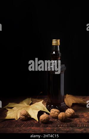 Eine Flasche Walnusswein auf einem Holztisch eingefügt, die Walnüsse und Blätter auf ihm hat Stockfoto