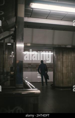 Vertikale Aufnahme eines Mannes, der in einem Bahnhof auf einen Zug wartet Stockfoto