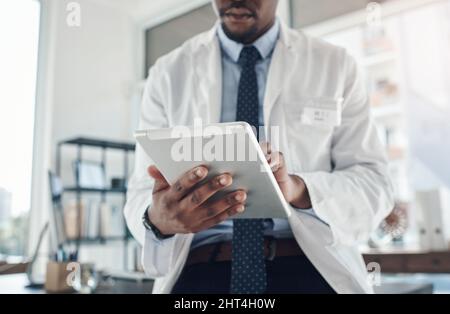 Jetzt kann ich Informationen auf dem Bildschirm abrufen. Aufnahme eines nicht erkennbaren Arztes mit einem digitalen Tablet in einem Büro. Stockfoto