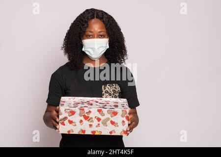 Junge afrikanische Frau mit Gesichtsmaske und Geschenk Stockfoto