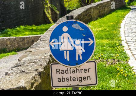 Schmutziges Straßenschild von Mutter und Kind für die Demontage des Radfahrers in deutscher Sprache an einem sonnigen Tag Stockfoto