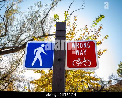 Blaue und rote Schilder auf Holzpfosten, die darauf hindeuten, dass Wanderer weitermachen können, aber für Fahrradfahrer ein falscher Weg. Stockfoto