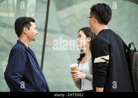 Drei junge asiatische Menschen stehen und unterhalten sich glücklich und lächelnd auf der Straße Stockfoto