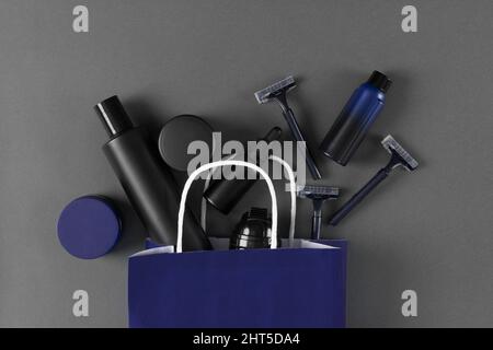 Hautpflegekosmetik für Männer in Papiertüte. Kosmetikprodukte für männliche Körperpflege auf grauem Hintergrund. Draufsicht, flach liegend Stockfoto