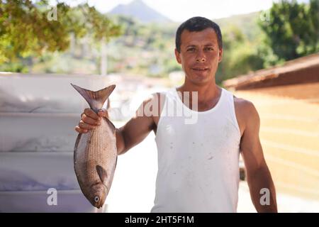 Zeigt seinen Fang. Porträt eines Fischers, der einen großen Fisch in der Hand hält, den er gefangen hat. Stockfoto