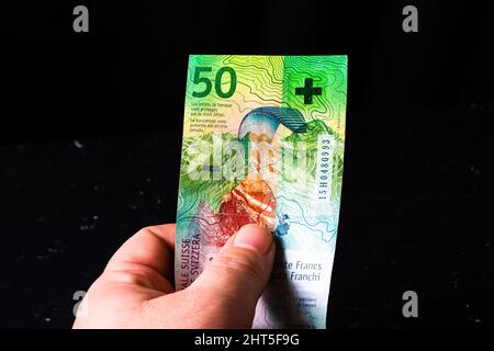 Nahaufnahme einer menschlichen Hand, die eine Schweizer Banknote von 50 auf einer schwarzen Oberfläche hält Stockfoto