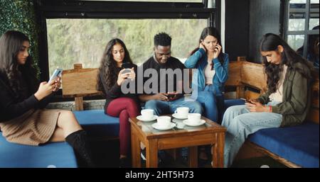 Eine Gruppe südasiatischer Freunde konzentrierte sich in einem Café in Indien auf ihre Smartphones Stockfoto