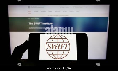 Person, die Mobiltelefon mit dem Logo des Banktransaktionssystems SWIFT auf dem Bildschirm vor der Webseite hält. Konzentrieren Sie sich auf die Telefonanzeige. Stockfoto