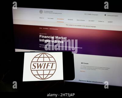 Person, die Smartphone mit dem Logo des Banktransaktionssystems SWIFT auf dem Bildschirm vor der Website hält. Konzentrieren Sie sich auf die Telefonanzeige. Stockfoto