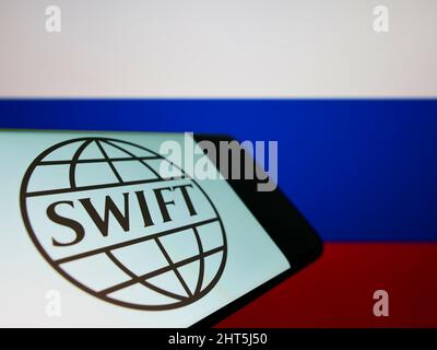 Mobiltelefon mit Logo des Banktransaktionssystems SWIFT auf dem Bildschirm vor der Nationalflagge der Russischen Föderation. Konzentrieren Sie sich auf die Telefonanzeige. Stockfoto