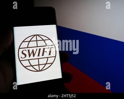 Person, die das Smartphone mit dem Logo des Banktransaktionssystems SWIFT auf dem Bildschirm vor der russischen Nationalflagge hält. Konzentrieren Sie sich auf die Telefonanzeige. Stockfoto
