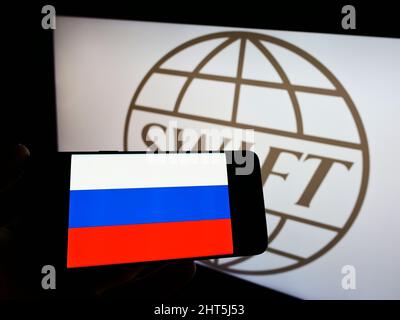 Person hält Smartphone mit Flagge Russlands auf dem Bildschirm vor dem Logo des Banküberweisungssystems SWIFT. Konzentrieren Sie sich auf die Telefonanzeige. Stockfoto
