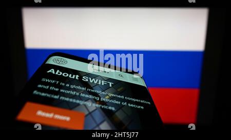 Handy mit Webseite des Banktransaktionssystems SWIFT auf dem Bildschirm vor der russischen Flagge. Konzentrieren Sie sich auf die Telefonanzeige. Stockfoto