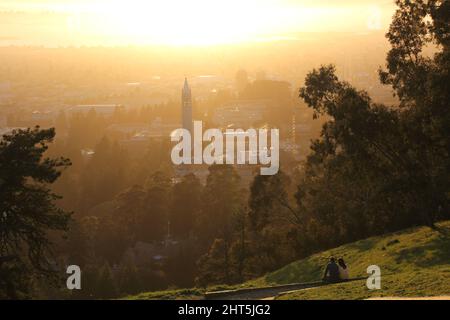 Paar sitzen auf dem Gras in der Nähe des Berkeley campanile (Sather Tower) bei Sonnenuntergang in Kalifornien, USA Stockfoto