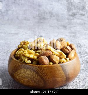 Nahaufnahme einer Vielzahl von Nüssen in einer Holzschale auf einem verschwommenen grauen Hintergrund Stockfoto