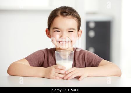 Gesunde Knochen, glückliche Kinder. Portrait eines niedlichen kleinen Mädchens, das ein Glas Milch genießt. Stockfoto