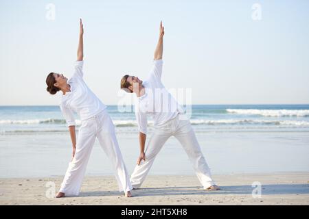 Yoga am Meer. Ein junges Paar, das am Strand Yoga praktiziert. Stockfoto