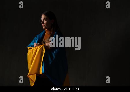 Traurige Frau mit Ukraine-Flagge bedeckt. Konzept des Stehens mit der ukrainischen Nation im Krieg mit Russland. Stockfoto