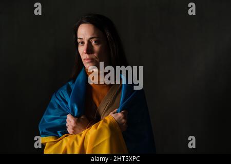 Traurige Frau mit Ukraine-Flagge bedeckt. Konzept des Stehens mit der ukrainischen Nation im Krieg mit Russland. Stockfoto