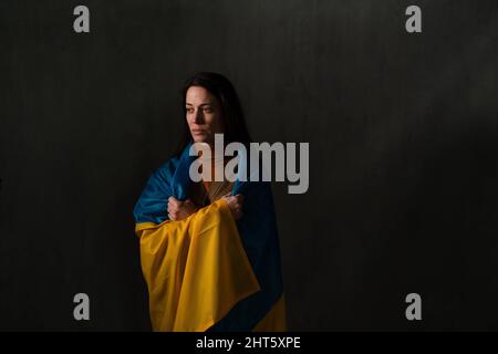 Traurige Frau mit Ukraine-Flagge bedeckt. Konzept des Stehens mit der ukrainischen Nation im Krieg mit Russland. Stockfoto