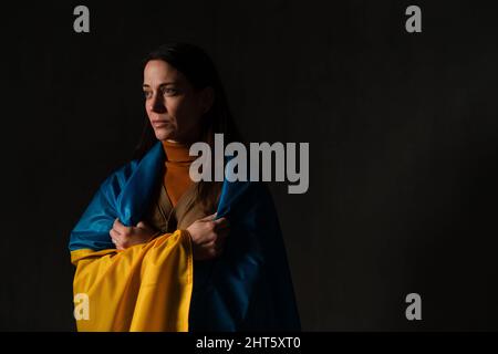 Traurige Frau mit Ukraine-Flagge bedeckt. Konzept des Stehens mit der ukrainischen Nation im Krieg mit Russland. Stockfoto