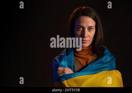 Traurige Frau mit Ukraine-Flagge bedeckt. Konzept des Stehens mit der ukrainischen Nation im Krieg mit Russland. Stockfoto