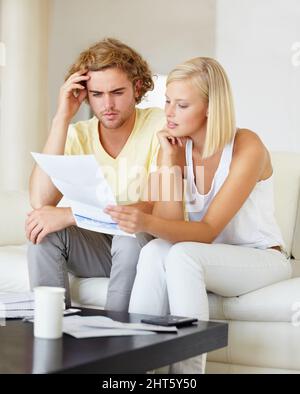 Woher kommen all diese Rechnungen? Ein junges Paar, das zusammen in der Lounge einen Finanzbericht liest. Stockfoto