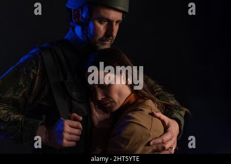 Traurige Frau, die sich von ihrem militärischen Ehemann verabschiedet, der im Krieg kämpfen wird, auf schwarzem Hintergrund. Stockfoto