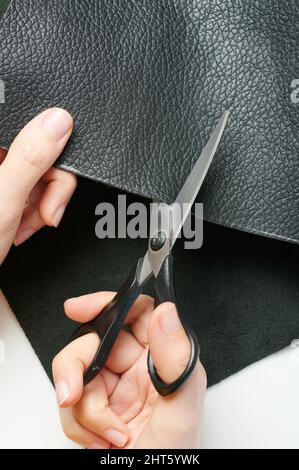 Thema „Beruf anpassen“. Hände mit Schere schneiden Stück aus schwarzem Leder Stockfoto