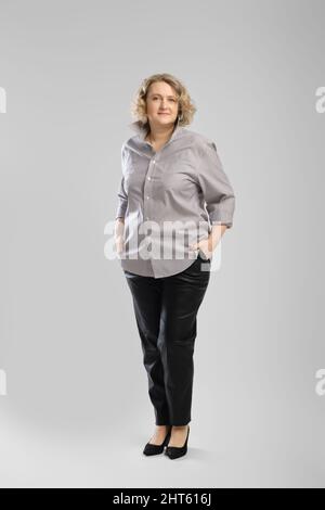 Ganzkörper-Casual-Porträt einer älteren Frau in grauem Hemd und Hose auf grauem Studiohintergrund Stockfoto