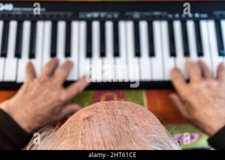 Aufnahme über dem Kopf von den Händen eines älteren Mannes, der eine musikalische Tastatur spielte Stockfoto