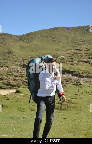 Ein fröhlicher junger Tourist, der mit einem Fallschirmrucksack in den Berg geht Stockfoto
